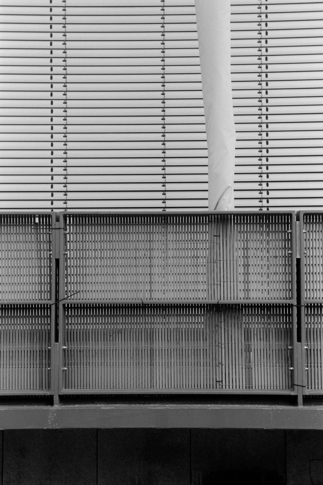 abstract black and white photography in portrait format. datail of a building with some kind of fence in foreground and other structures with vertical and horizontal lines.