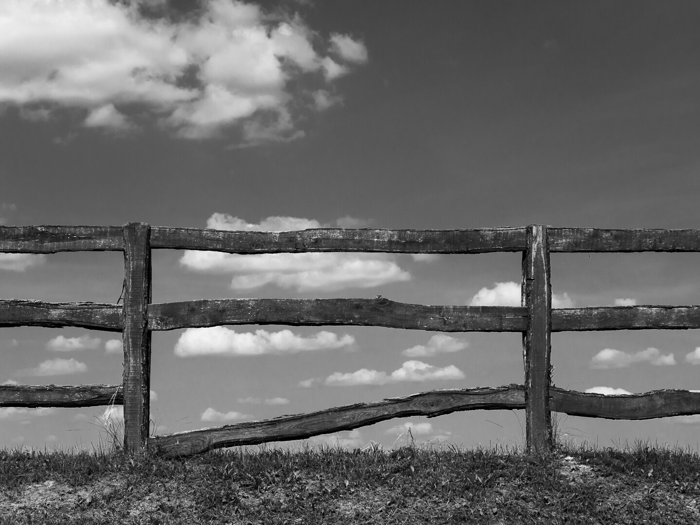 Ein Feld eines Ranchzaunes gegen Himmel mit weißen Wolken. Die unterste Querlatte hat sich links gelöst und liegt auf dem Boden auf. Ein Feld eines Ranchzaunes gegen Himmel mit weißen Wolken. Die unterste Querlatte hat sich links gelöst und liegt auf dem Boden auf.