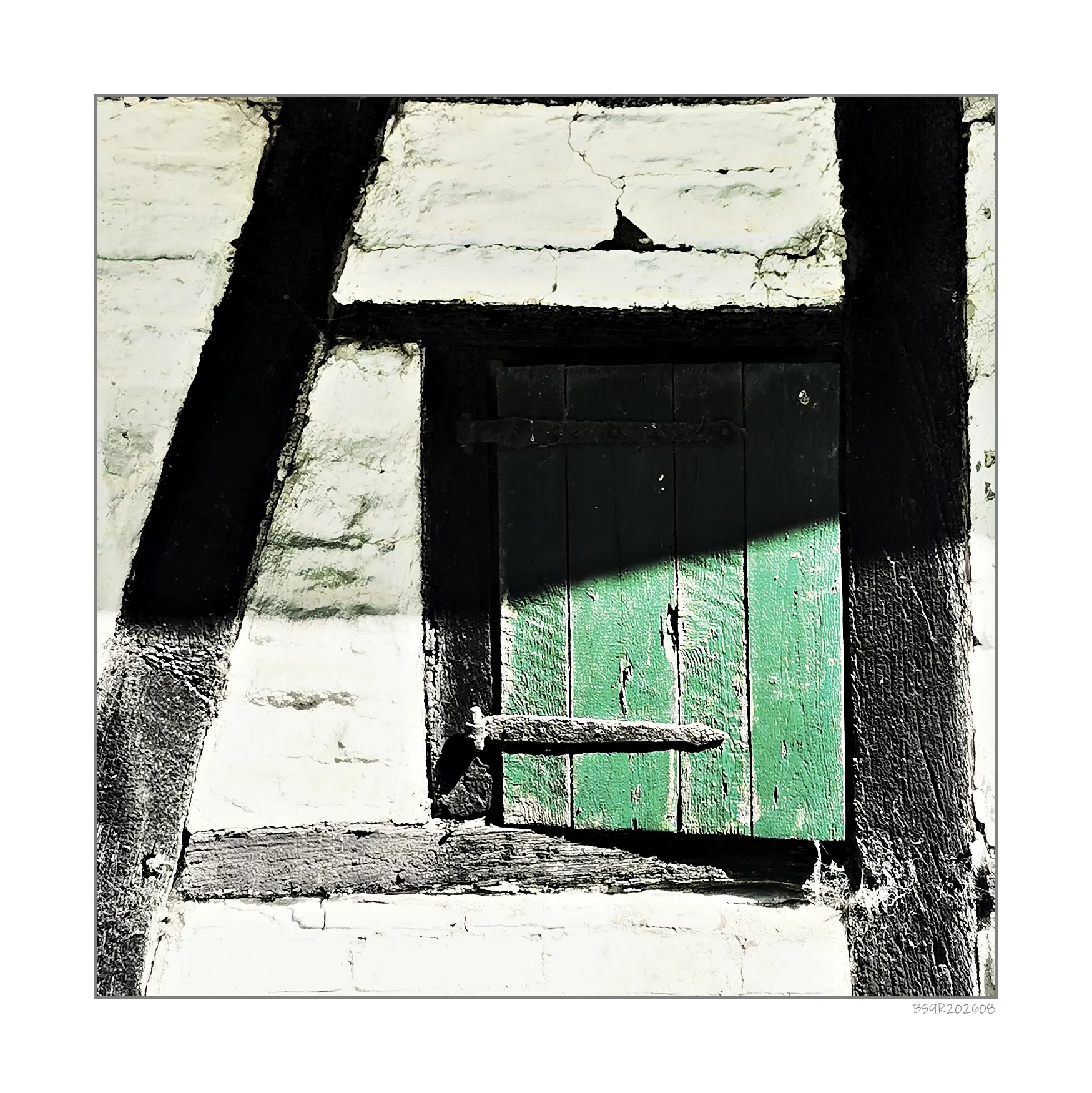 Ein kleines, grünes Fenster mit Holzläden ist in eine weiß verputzte Fachwerkwand eingelassen. Die dunklen Holzbalken verlaufen schräg und rahmen das Fenster ein. Ein schräger Schatten fällt über die Fensterläden und einen Teil der Wand. Die Struktur des Putzes und die Maserung des Holzes sind deutlich erkennbar.